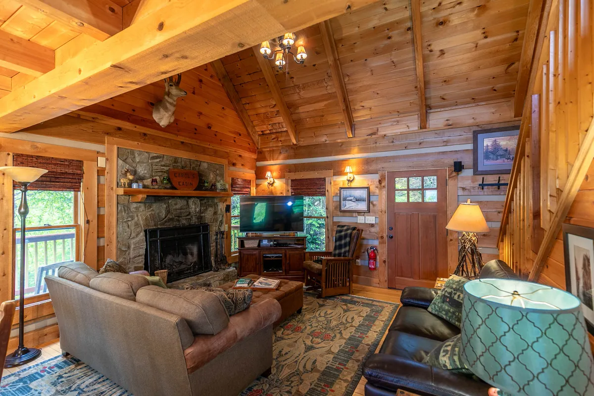 A welcoming living room showcasing a fireplace, television, wooden beams, a soft rug, and comfortable sofas arranged for conversation or relaxing. The morning sunlight brightens the space, enhancing its warmth and appeal for social gatherings and family movie nights.