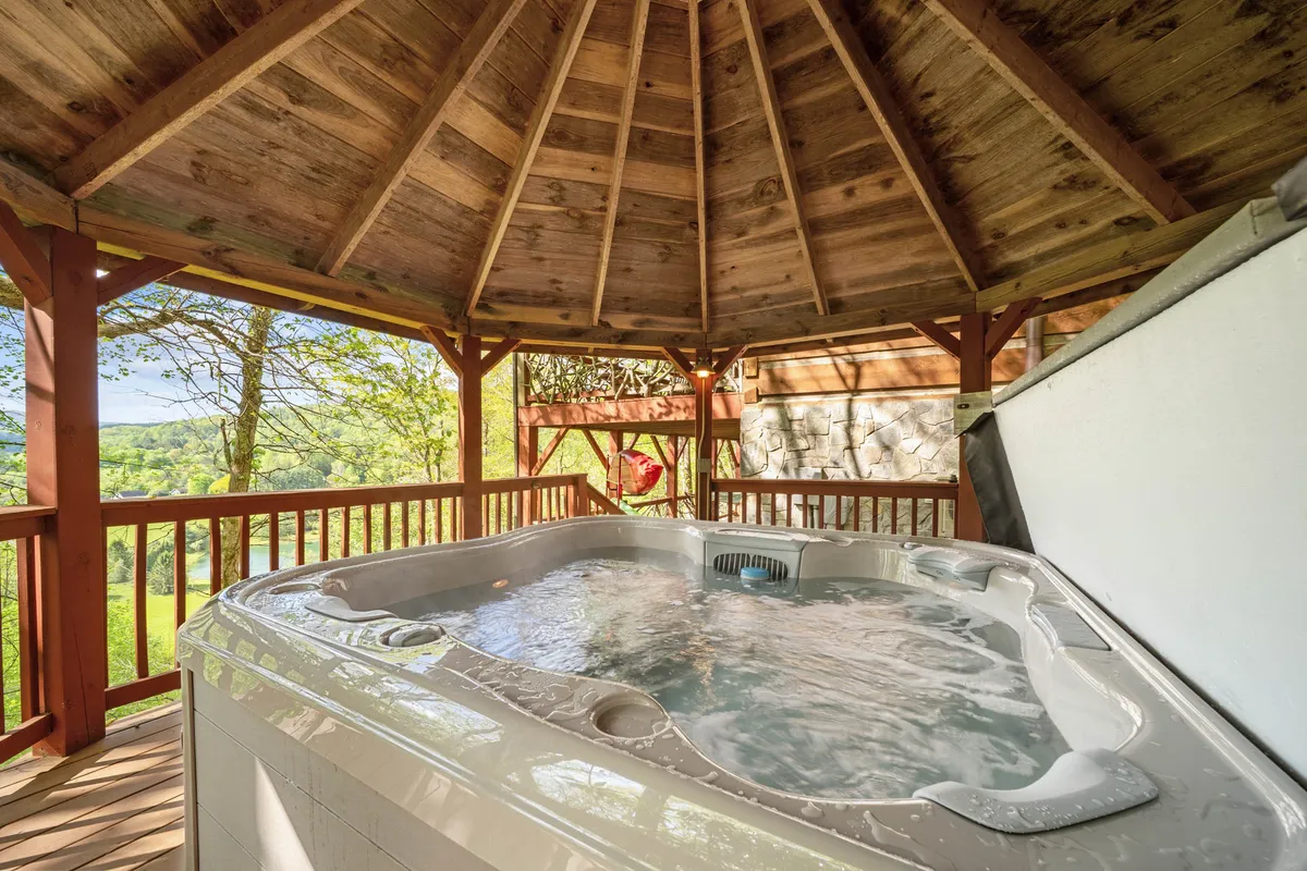 A tranquil hot tub is tucked under wooden beams, surrounded by lush greenery visible through large windows or an open side. The setup suggests privacy and comfort, ideal for starlit soaks. The scene is intimate, offering a sanctuary for relaxation after a day of exploring the Blue Ridge area.