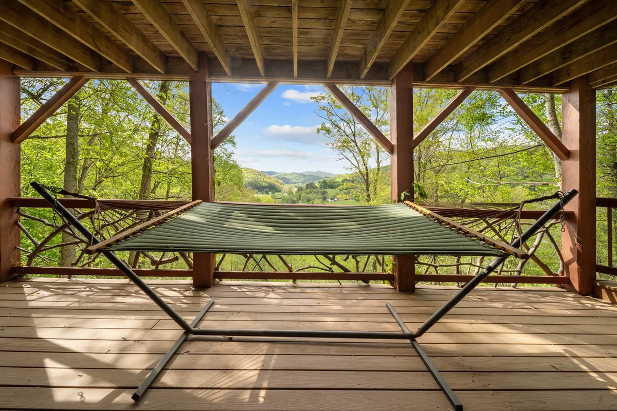 A cozy hammock is suspended under a wooden structure, framed by lush greenery and set against a picturesque mountain backdrop. The setting feels peaceful and private, inviting guests to unwind, read, or simply take in the views and fresh mountain air.