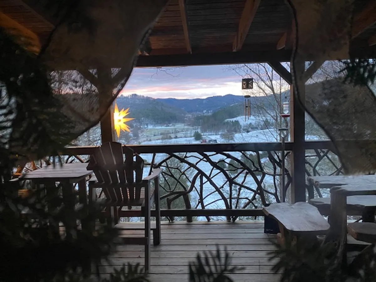 This image features a pair of wooden chairs set on a deck, with a decorative star accent and a sweeping mountain view in the background. The setting is serene, inviting, and perfectly suited for quiet moments shared by couples. The sky’s gentle gradient hints at either a sunrise or sunset, enhancing the romantic mood.