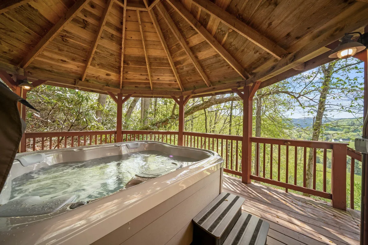 A hot tub sheltered under a wooden gazebo is surrounded by trees, offering privacy and a direct connection to nature. The inviting waters promise year-round relaxation with forest views, perfectly positioned for a soak after a day of adventure.