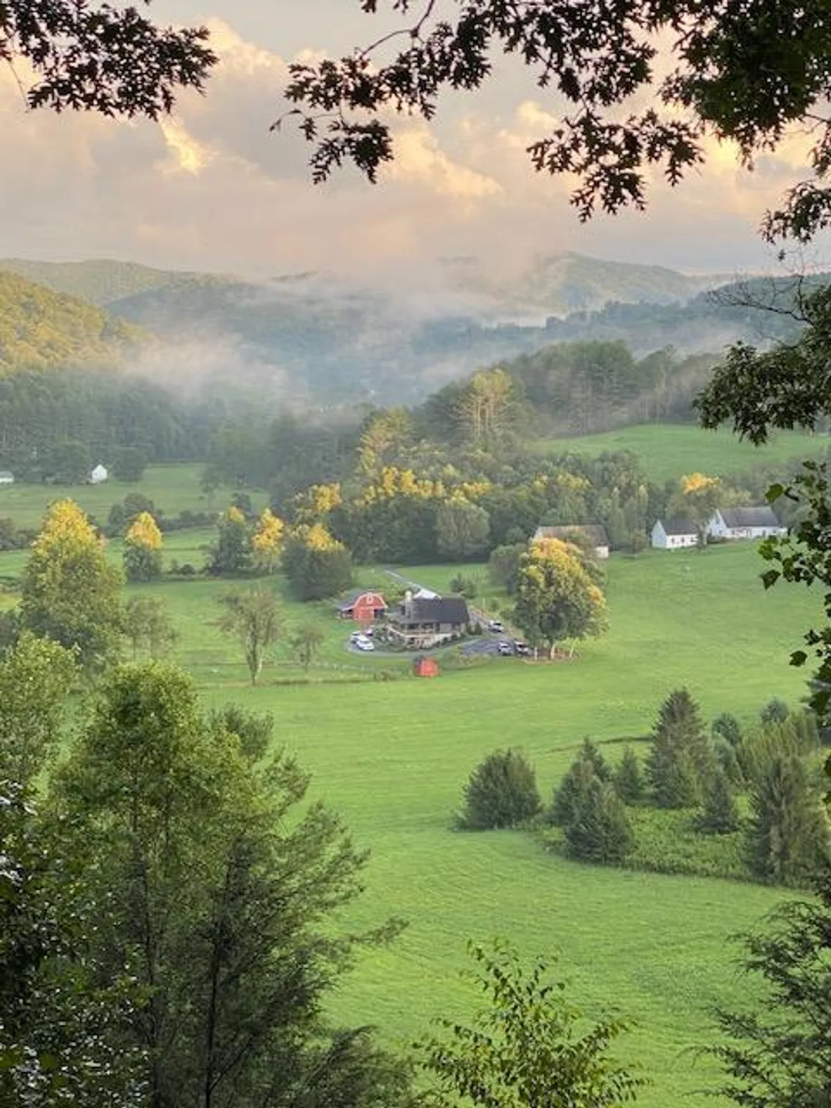 The image features a classic farmhouse and a striking red barn set amid rolling green fields with hills encircling the scene. The natural beauty is enhanced by wide-open spaces, lush grass, and a tranquil, peaceful mood. The image invites the viewer to imagine outdoor activities like hiking, picnicking, and exploring the land, with highlights on enjoying sunsets from the hilltop and stargazing at night.